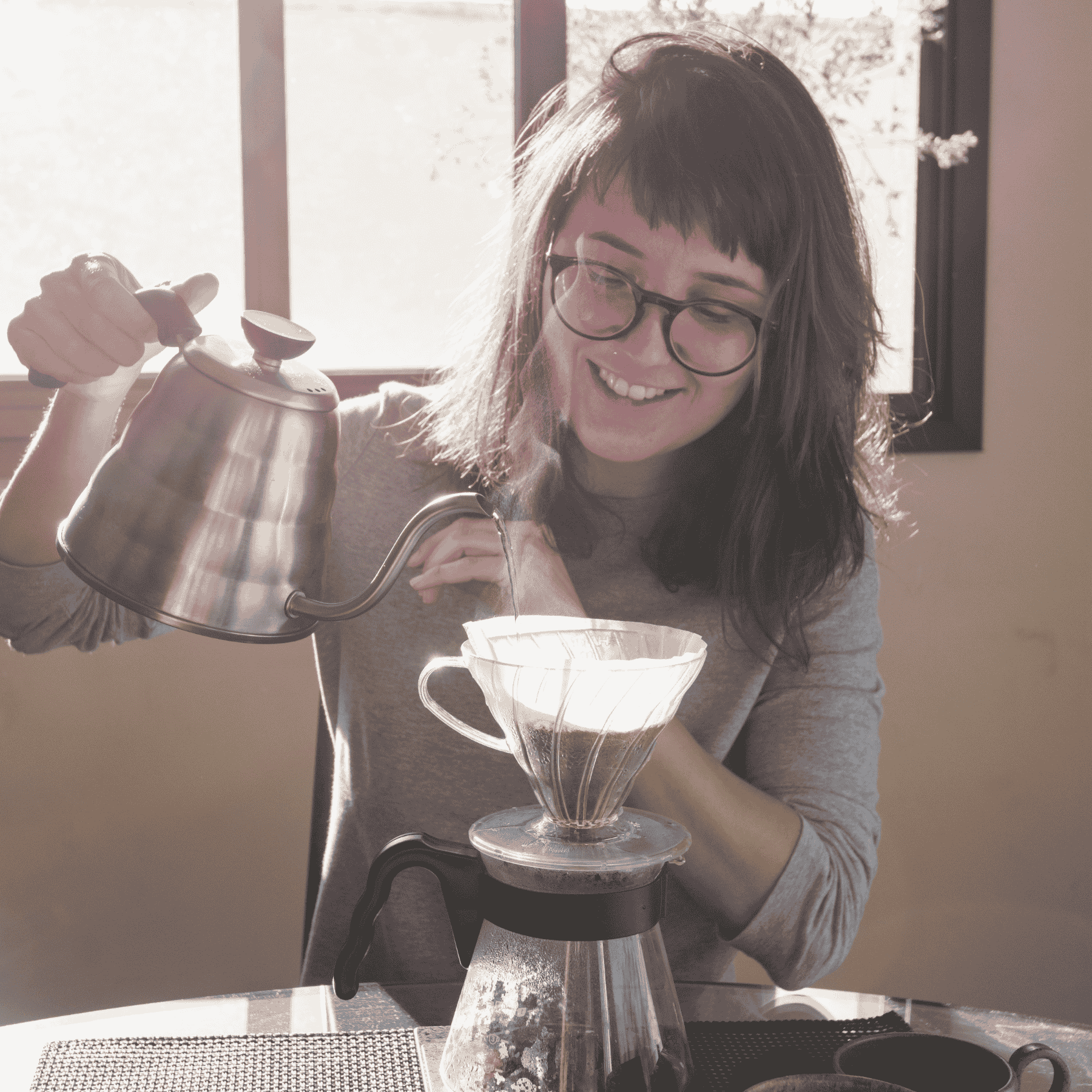 Smiling woman brewing coffee with a pour-over setup, demonstrating how roast level and brew method work together to shape flavor.