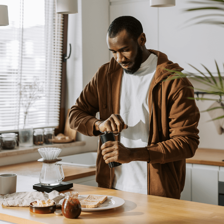 Man grinding coffee beans by hand in a cozy kitchen, preparing to brew a fresh cup of coffee at home.